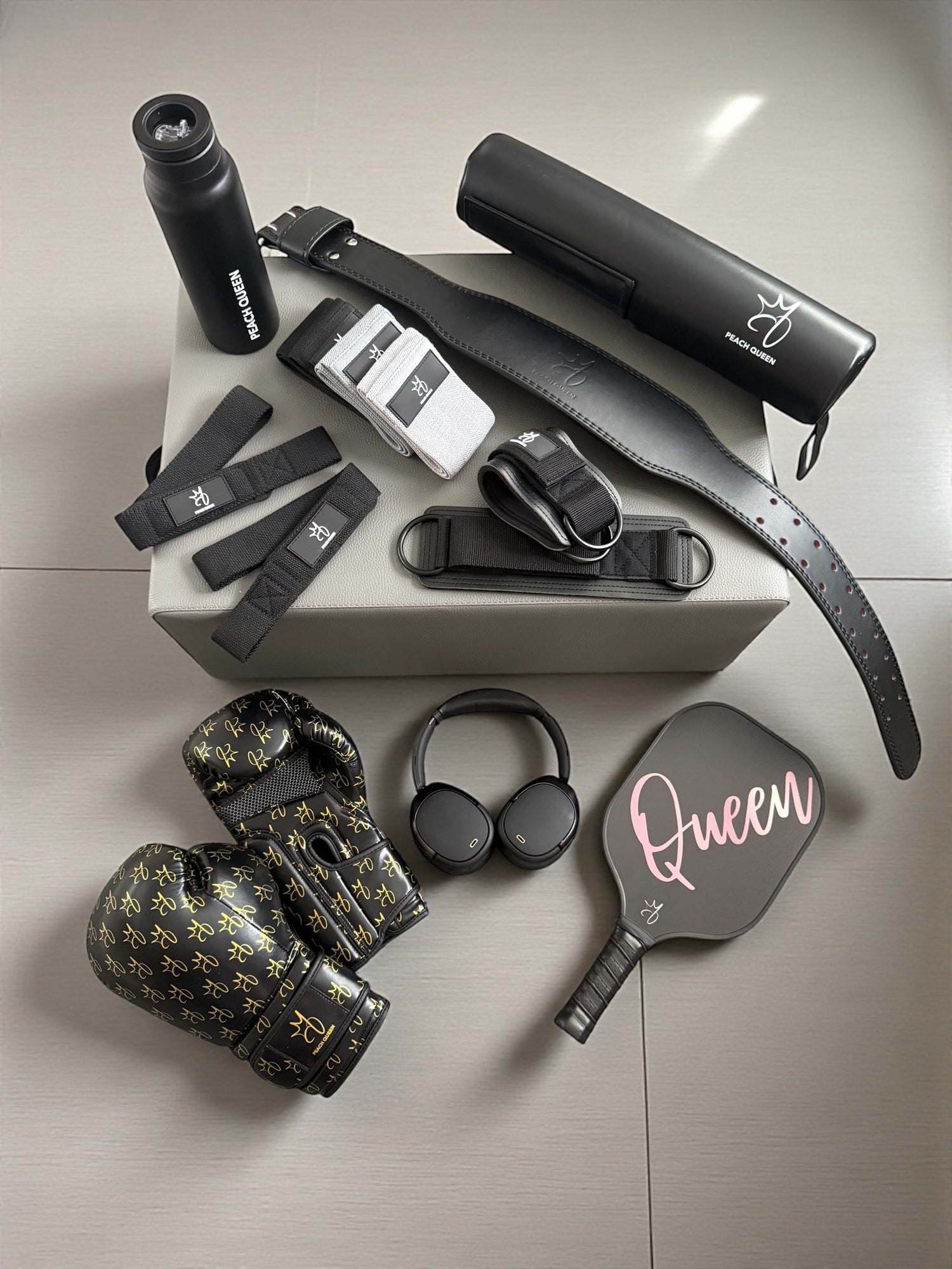 Boxing gloves and fitness gears such as barbell pad, resistance bands, lifting belt, lifting straps , ankle straps and pickleball paddle in black color, display in a light grey floor.